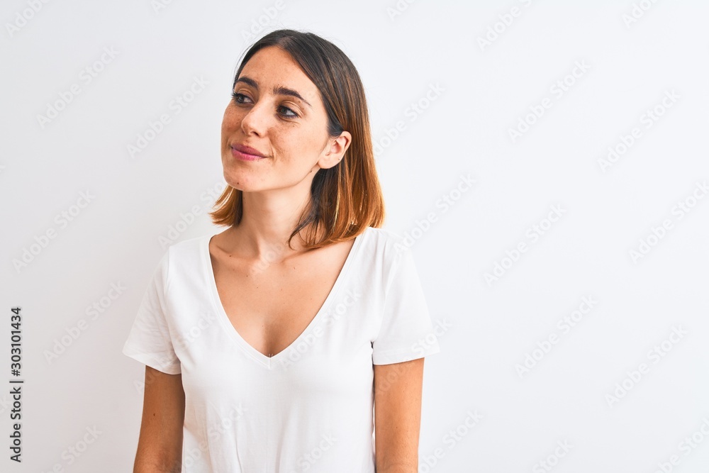 Beautiful redhead woman wearing casual white t-shirt over isolated background smiling looking to the side and staring away thinking. Beautiful redhead woman wearing casual white t-shirt over isolated background smiling looking to the side and staring away thinking.