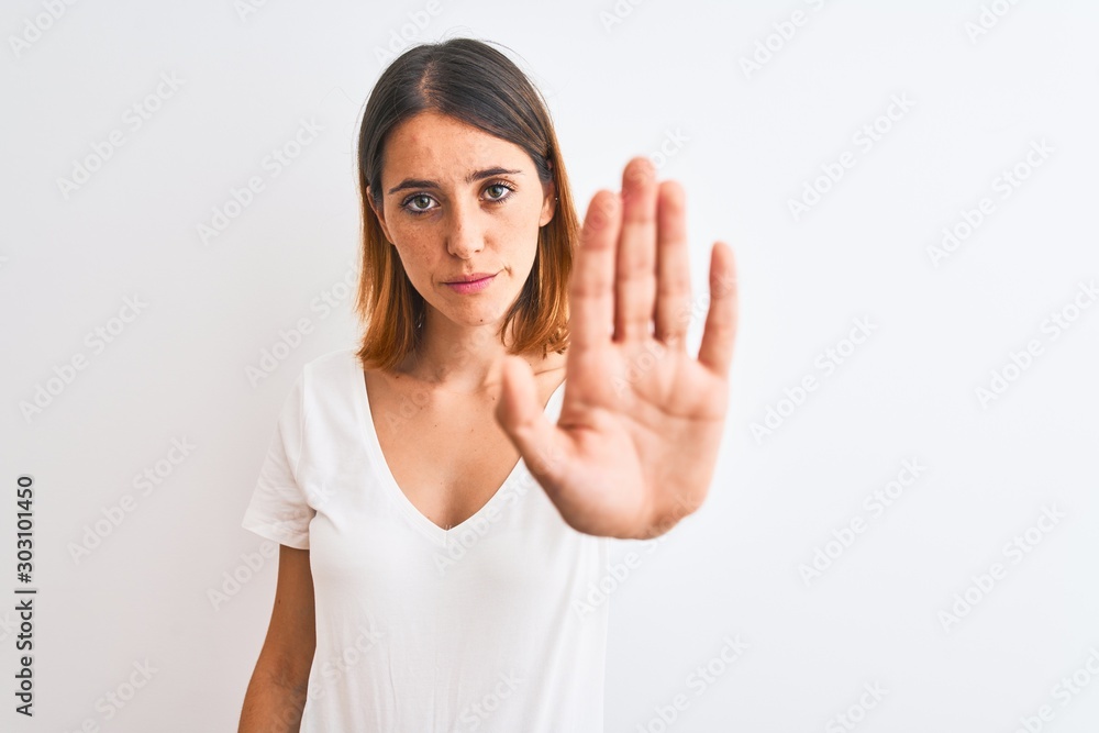 Beautiful redhead woman wearing casual white t-shirt over isolated background doing stop sing with palm of the hand. Warning expression with negative and serious gesture on the face. Beautiful redhead woman wearing casual white t-shirt over isolated background doing stop sing with palm of the hand. Warning expression with negative and serious gesture on the face.