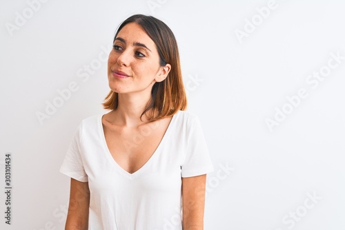 Beautiful redhead woman wearing casual white t-shirt over isolated background smiling looking to the side and staring away thinking. © Krakenimages.com