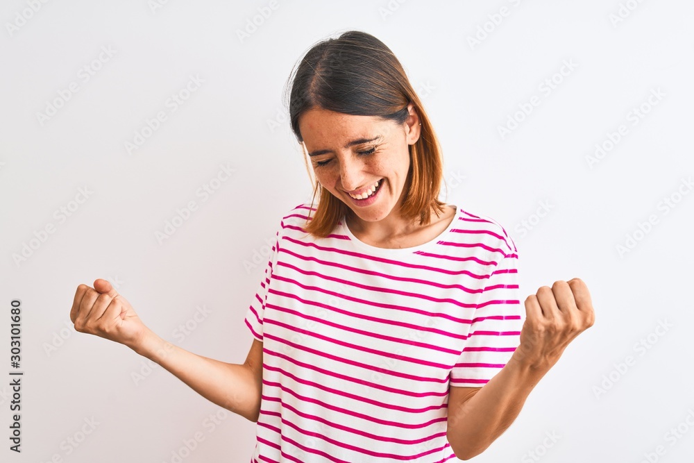 Beautiful redhead woman wearing casual striped pink t-shirt over isolated background very happy and excited doing winner gesture with arms raised, smiling and screaming for success. Celebration Beautiful redhead woman wearing casual striped pink t-shirt over isolated background very happy and excited doing winner gesture with arms raised, smiling and screaming for success. Celebration