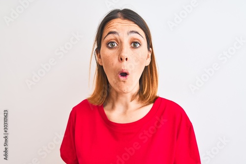 Beautiful redhead woman wearing casual red t-shirt over isolated background afraid and shocked with surprise expression, fear and excited face.