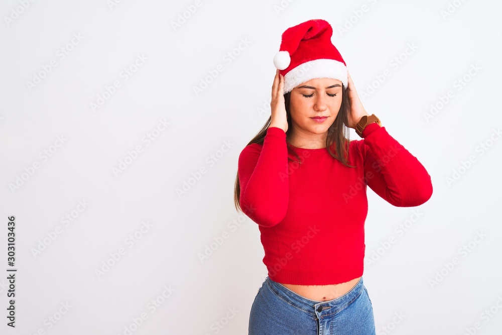Young beautiful girl wearing Christmas Santa hat standing over isolated white background with hand on head for pain in head because stress. Suffering migraine.