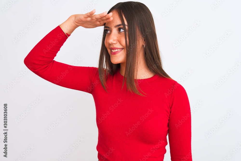 Young beautiful girl wearing red casual t-shirt standing over isolated white background very happy and smiling looking far away with hand over head. Searching concept. Young beautiful girl wearing red casual t-shirt standing over isolated white background very happy and smiling looking far away with hand over head. Searching concept.