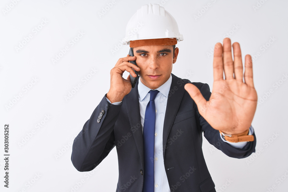 Young architect man wearing helmet talking on smartphone over isolated white background with open hand doing stop sign with serious and confident expression, defense gesture Young architect man wearing helmet talking on smartphone over isolated white background with open hand doing stop sign with serious and confident expression, defense gesture