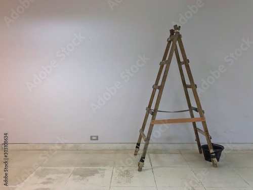 The wooden ladder and black bucket are placed on the floor for repairing at the construction site with the white background.