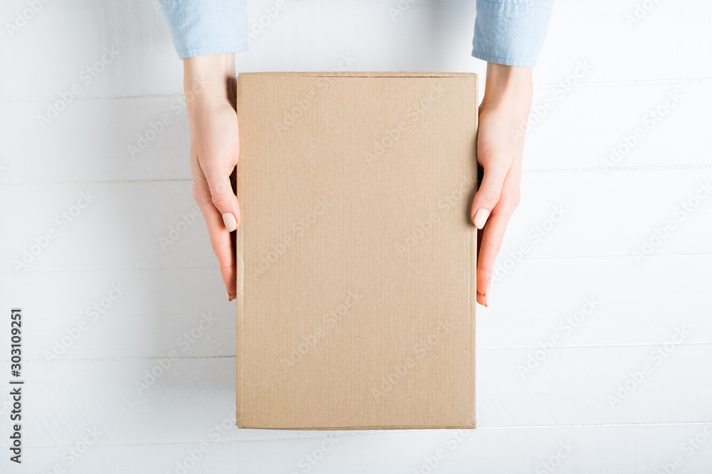Rectangular cardboard box in female hands. Top view, white background - obrazy, fototapety, plakaty 