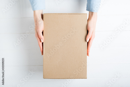 Rectangular cardboard box in female hands. Top view, white background