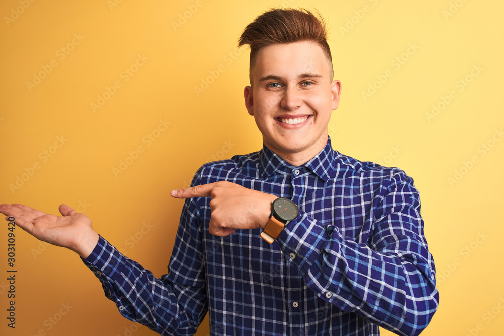Young handsome man wearing casual shirt standing over isolated yellow background amazed and smiling to the camera while presenting with hand and pointing with finger. Young handsome man wearing casual shirt standing over isolated yellow background amazed and smiling to the camera while presenting with hand and pointing with finger.