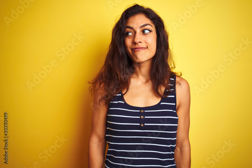 Young beautiful woman wearing striped t-shirt standing over isolated yellow background smiling looking to the side and staring away thinking.