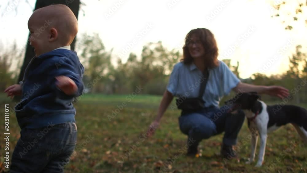 Cheerful kid toddler plays with a dog in the autumn park. Next to him is his happy mother. Childrens emotions Cheerful kid toddler plays with a dog in the autumn park. Next to him is his happy mother. Childrens emotions