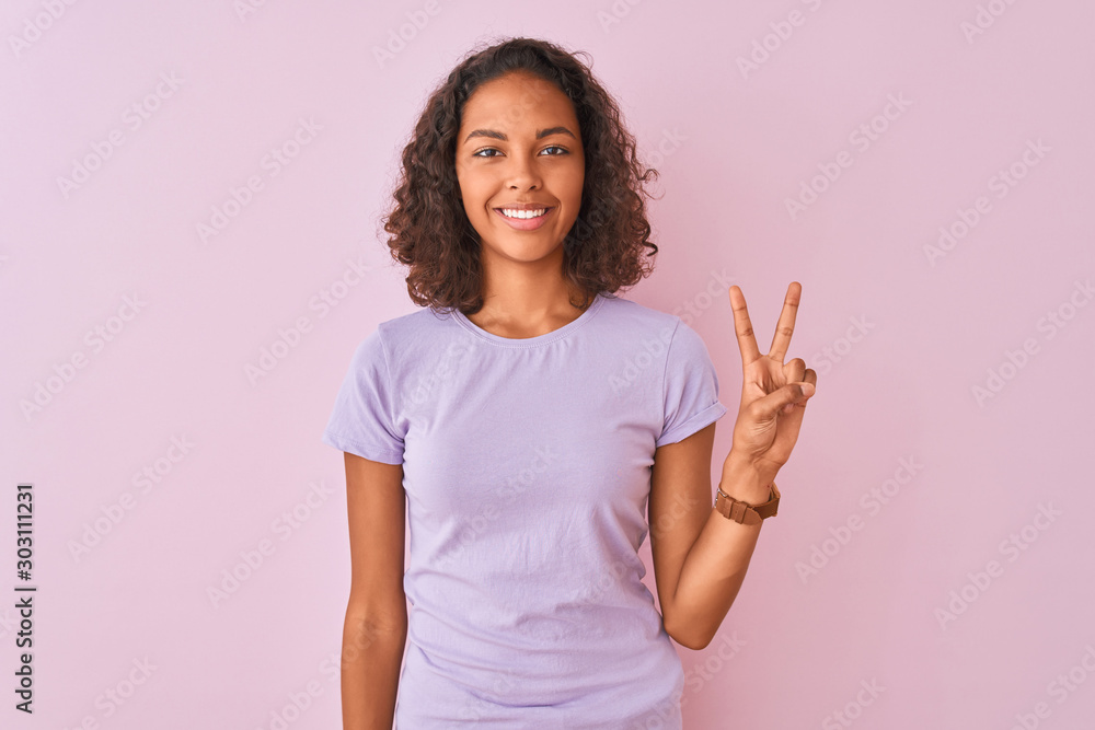 Young brazilian woman wearing t-shirt standing over isolated pink background showing and pointing up with fingers number two while smiling confident and happy. Young brazilian woman wearing t-shirt standing over isolated pink background showing and pointing up with fingers number two while smiling confident and happy.