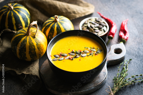 Homemade pumpkin cream soup with  seeds, spices and herbs on a dark background top view.