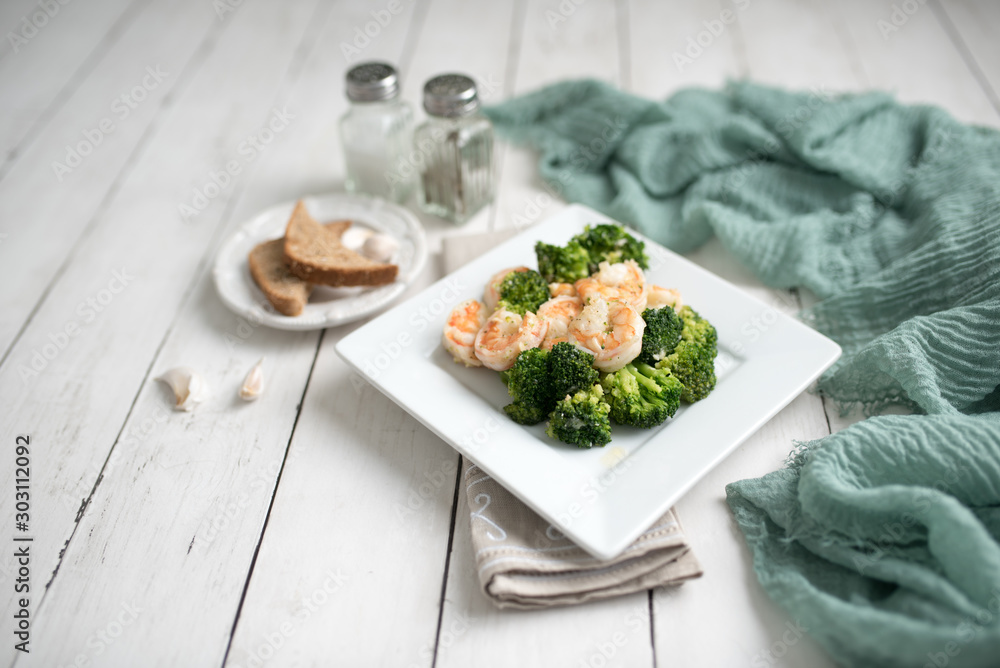 Healthy stir fry with shrimp broccoli and garlic on a white wood table