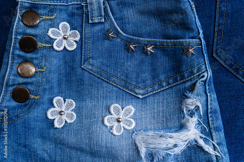 Denim Fabric pattern blue Jeans old ripped torn vintage fashion design decoration by white flowers and buttons background Jean texture closeup soft focus.
