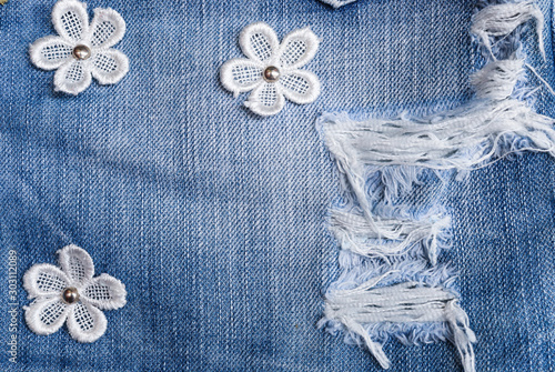 Denim Fabric pattern blue Jeans old ripped torn vintage fashion design decoration by white flowers and buttons background Jean texture closeup soft focus.