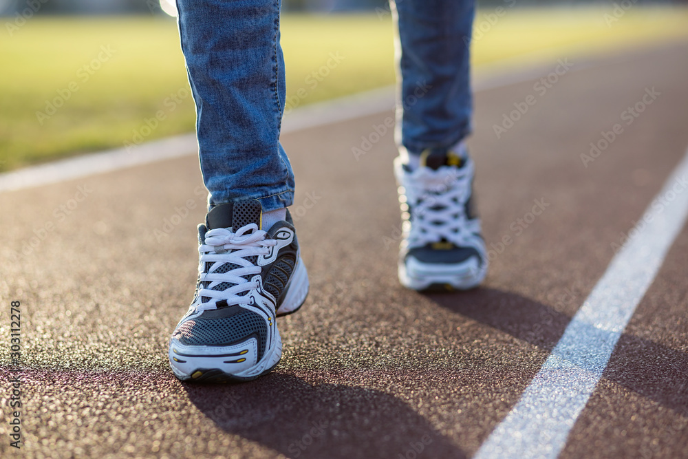Close up of woman feet in sport sneakers and blue jeans on running lane on outdoor sports court.