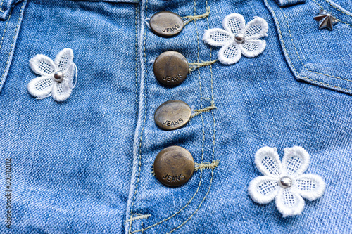 Denim Fabric pattern blue Jeans old ripped torn vintage fashion design decoration by white flowers and buttons background Jean texture closeup soft focus.