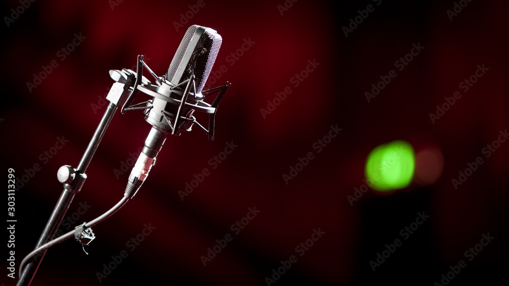 Recording light on green. Shallow focus on a stand mounted condenser microphone with a green recording light showing in the background blur.