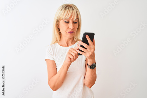 Middle age woman using smartphone standing over isolated white background with a confident expression on smart face thinking serious