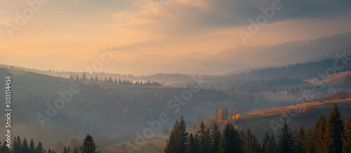 Beautiful autumn scenery panorama of foggy valley at Carpathian mountains at early morning before sunrise. Wide angle shot of misty hills at sunrise.