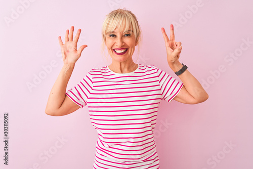 Middle age woman wearing striped t-shirt standing over isolated pink background showing and pointing up with fingers number seven while smiling confident and happy.