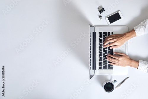 Slika na platnu A man is typing on laptop keyboard on modern white office desk, top view