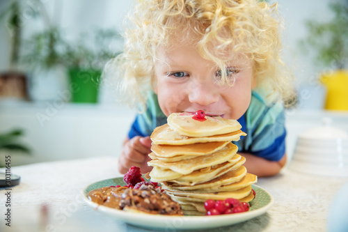 Leinwand Poster Little curly boy eating sweet pancakes