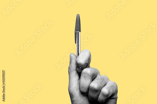 Concept of freedom of speech and information, stop censorship. Hand holding a pen in sign of protest, the pressure of censorship. Yellow background. Black and white image photo