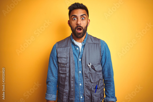 Fotografia Handsome indian technician man wearing uniform over isolated yellow background afraid and shocked with surprise expression, fear and excited face