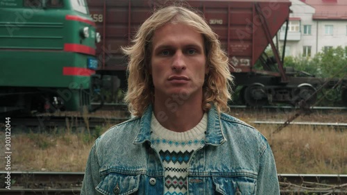 portrait of handsome blue-eyed guy with blond long curly hair on the background of the moving train photo