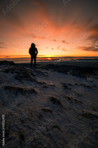 Hiker is standing on a Mountain Peak watching the Sunrise in Winter