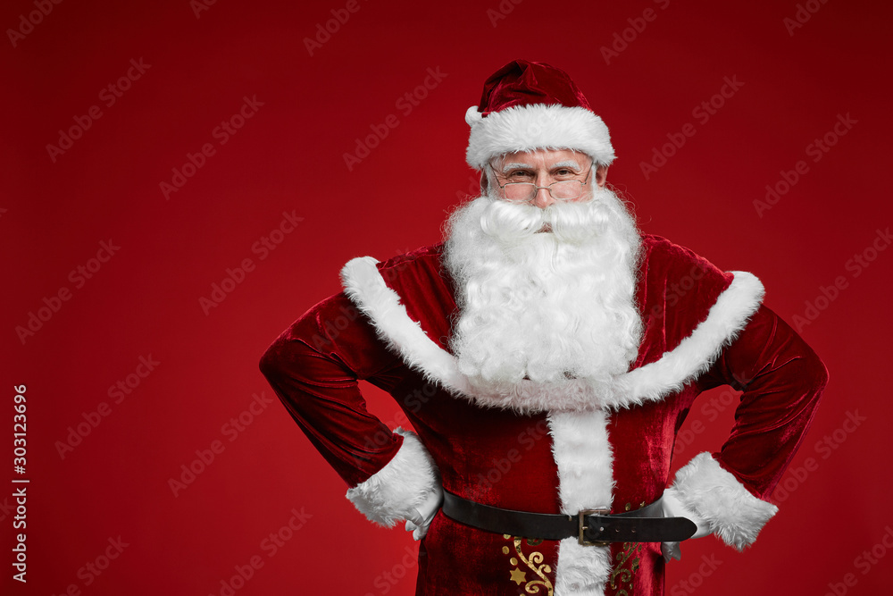 Portrait of happy Santa Claus in red costume and with white beard smiling at camera over red background