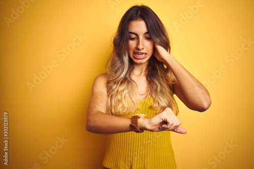 Young beautiful woman wearing t-shirt over yellow isolated background Looking at the watch time worried, afraid of getting late