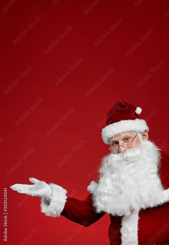 Portrait of Santa Claus making an advertisement and looking at camera isolated on red background