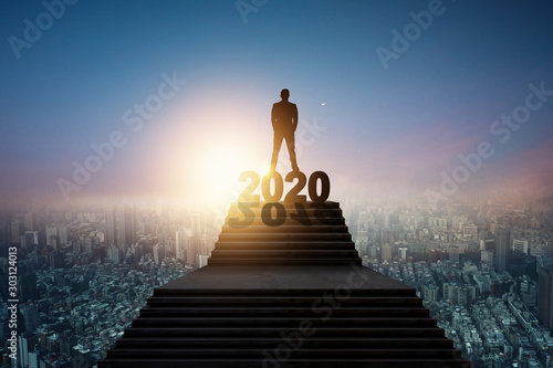 Success and leader of future concept, silhouette of businessman standing on 2020 new year letter on top of stair and looking over city