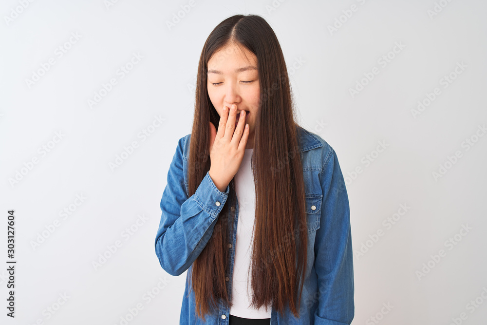 Young chinese woman wearing denim shirt standing over isolated white background bored yawning tired covering mouth with hand. Restless and sleepiness. Young chinese woman wearing denim shirt standing over isolated white background bored yawning tired covering mouth with hand. Restless and sleepiness.