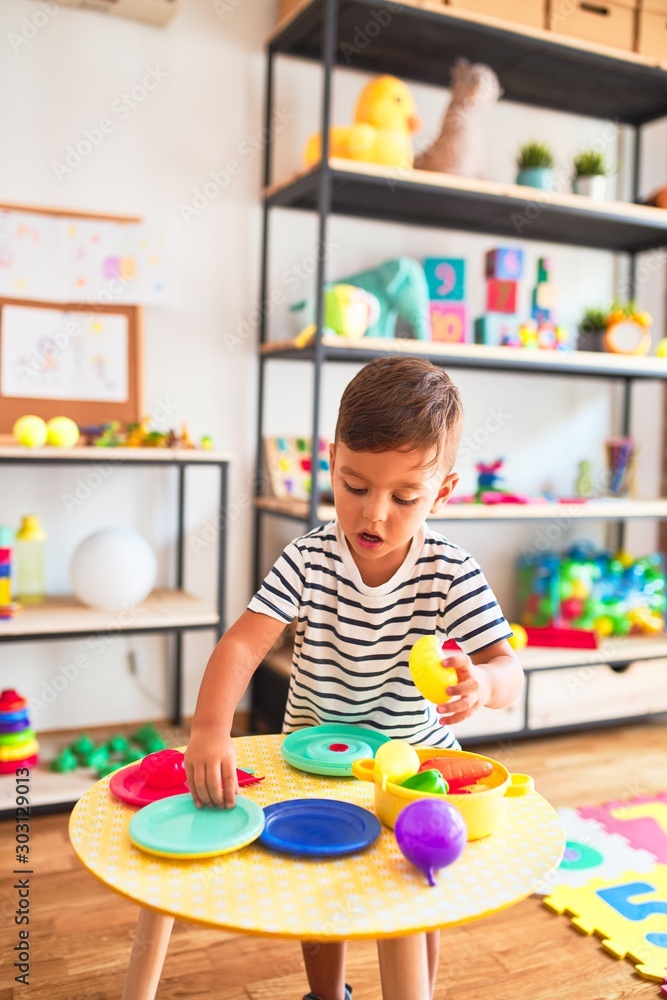 Beautiful toddler boy playing meals with plastic plates, fruits and vegetables at kindergarten Beautiful toddler boy playing meals with plastic plates, fruits and vegetables at kindergarten