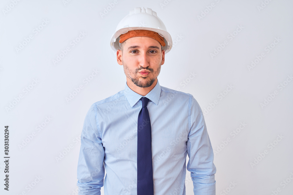 Young business man wearing contractor safety helmet over isolated background puffing cheeks with funny face. Mouth inflated with air, crazy expression. Young business man wearing contractor safety helmet over isolated background puffing cheeks with funny face. Mouth inflated with air, crazy expression.