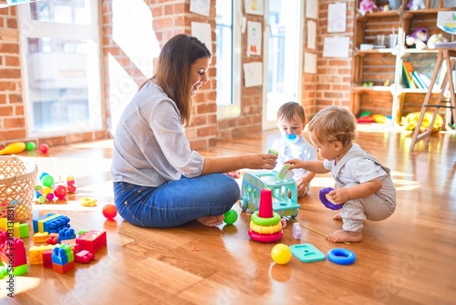 Foto Beautiful teacher and toddlers playing around lots of toys at kindergarten