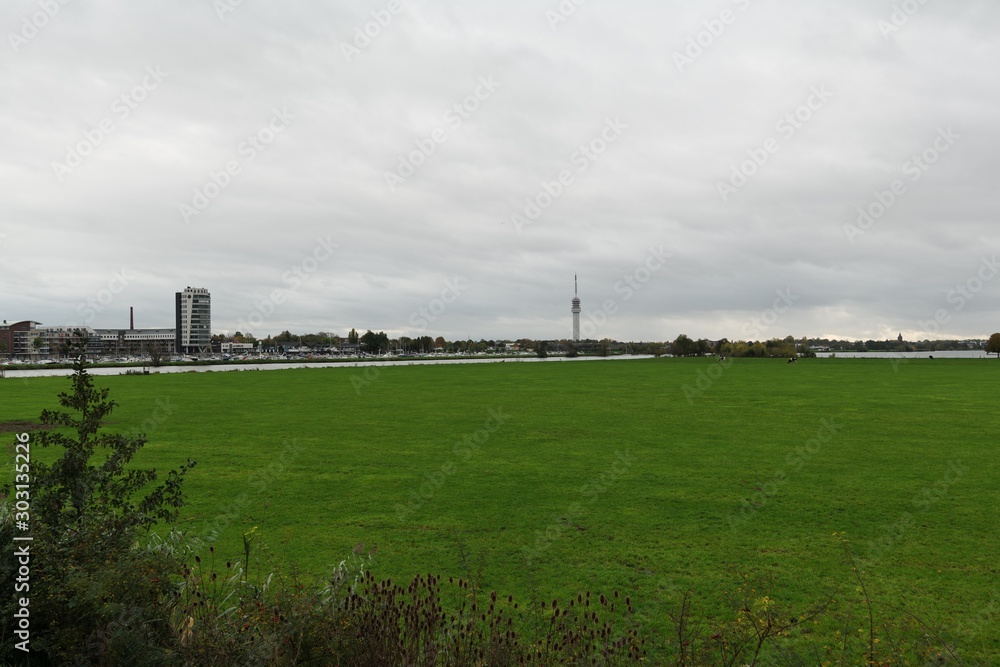 View over the the meadows from the lake Maasplassen to the horizon, in the background tower and the ports, the city skyline, dramatic sky, view towards Roermond, Limburg , Netherlands.