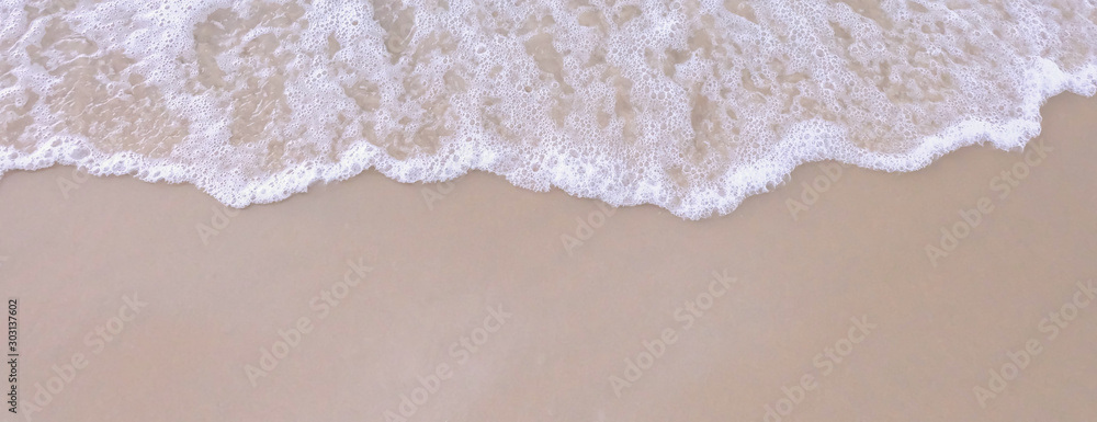summer background - soft wave with white bubbles on sandy beach