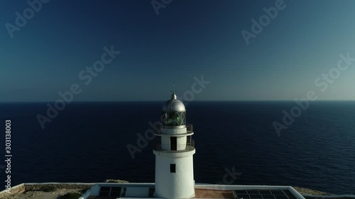 4K drone footage of a circular drone flight back over a white lighthouse the edge of a cliff in the morning in Menorca