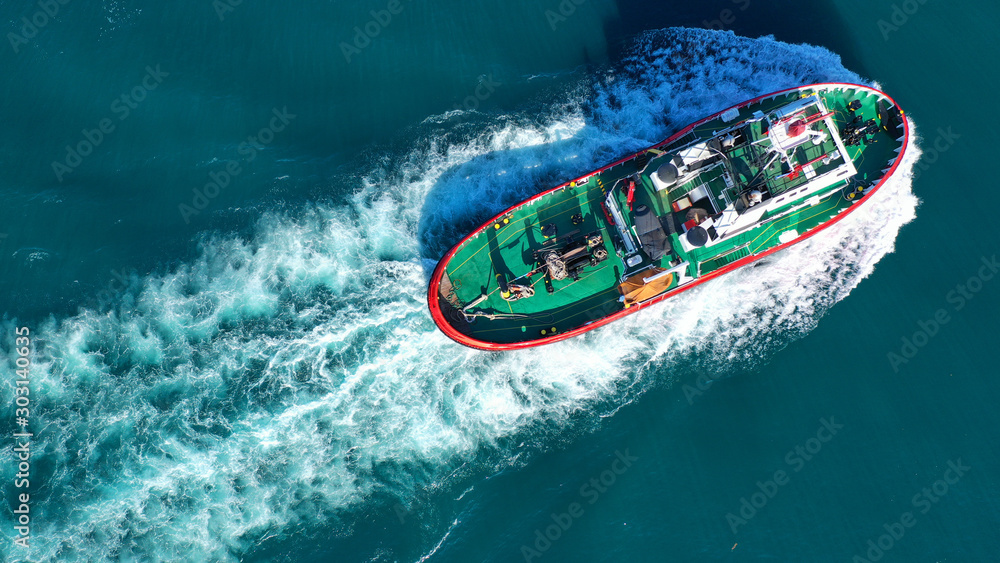 Aerial drone photo of tug boat cruising in high speed near cruise liner docked in Mediterranean port Aerial drone photo of tug boat cruising in high speed near cruise liner docked in Mediterranean port