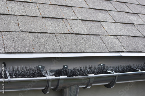 Plastic guard brush in new dark grey plastic rain gutter on asphalt shingles roof. photo