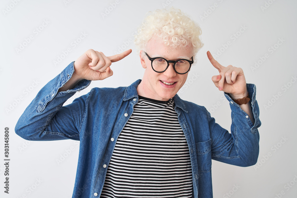 Young albino blond man wearing denim shirt and glasses over isolated white background smiling pointing to head with both hands finger, great idea or thought, good memory