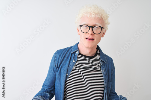Young albino blond man wearing denim shirt and glasses over isolated white background clueless and confused with open arms, no idea concept.
