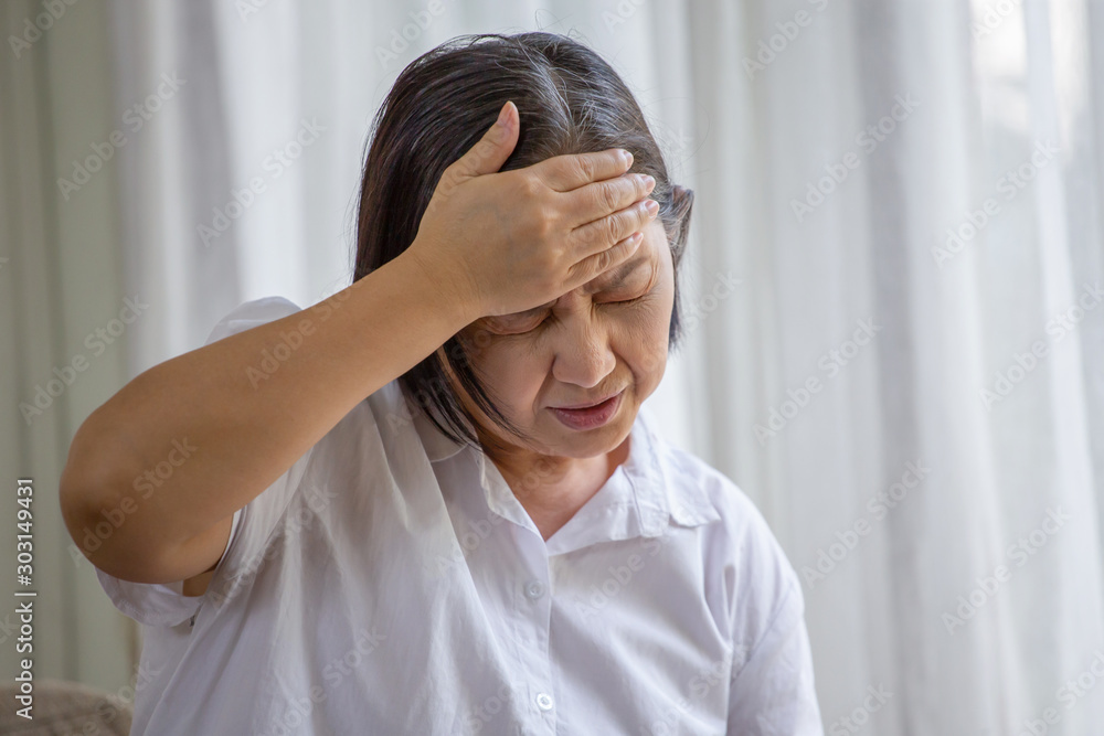 Asian senior woman sitting on sofa having headache at home. old female   stressed dizzy . elderly touching her head with her hands while having migraine or alzheimer .memory loss . indoor. copy space - obrazy, fototapety, plakaty 