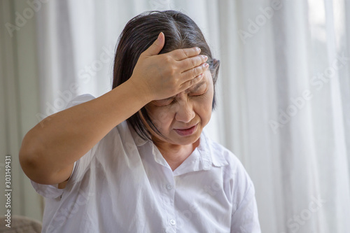 Asian senior woman sitting on sofa having headache at home. old female   stressed dizzy . elderly touching her head with her hands while having migraine or alzheimer .memory loss . indoor. copy space