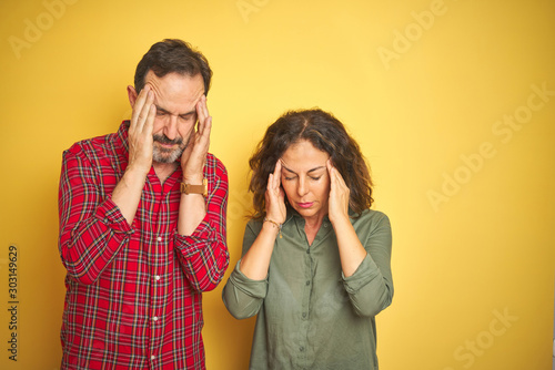 Beautiful middle age couple over isolated yellow background with hand on head for pain in head because stress. Suffering migraine.