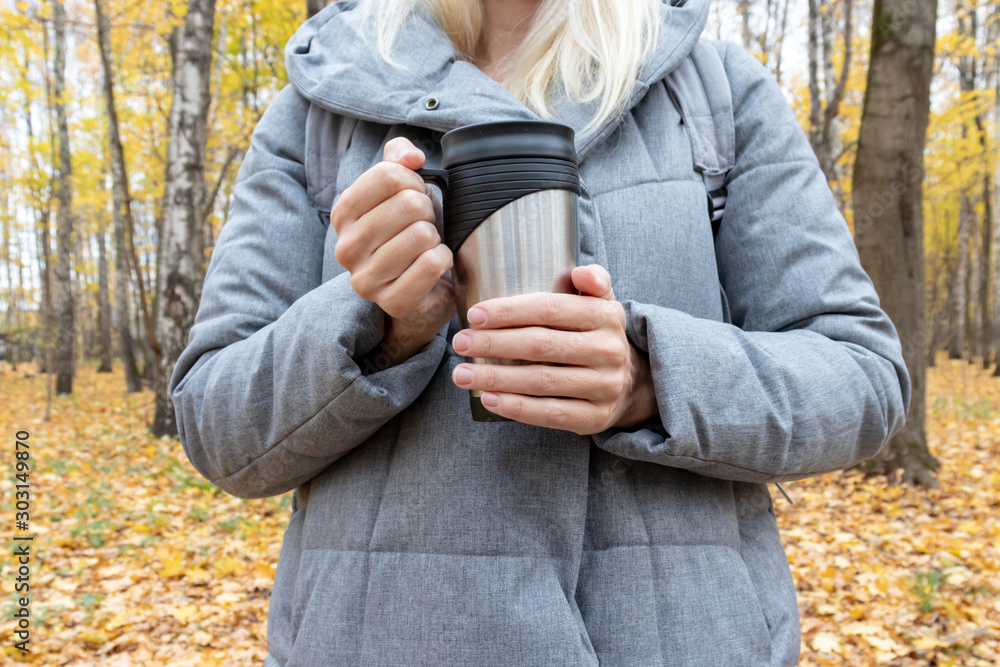 A young woman standing in colorful autumn park and holding a metal thermo cup with hot beverage A young woman standing in colorful autumn park and holding a metal thermo cup with hot beverage
